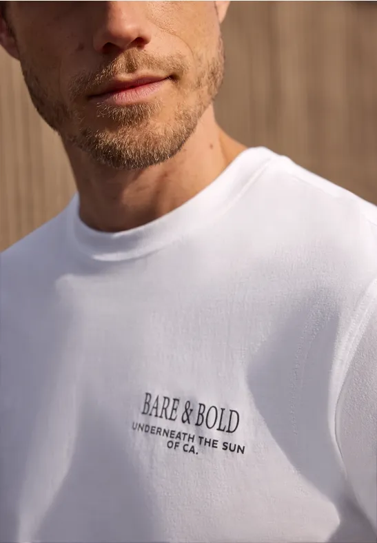 Nahaufnahme eines Mannes im weißen T-Shirt mit schwarzem Schriftzug auf der Brust.