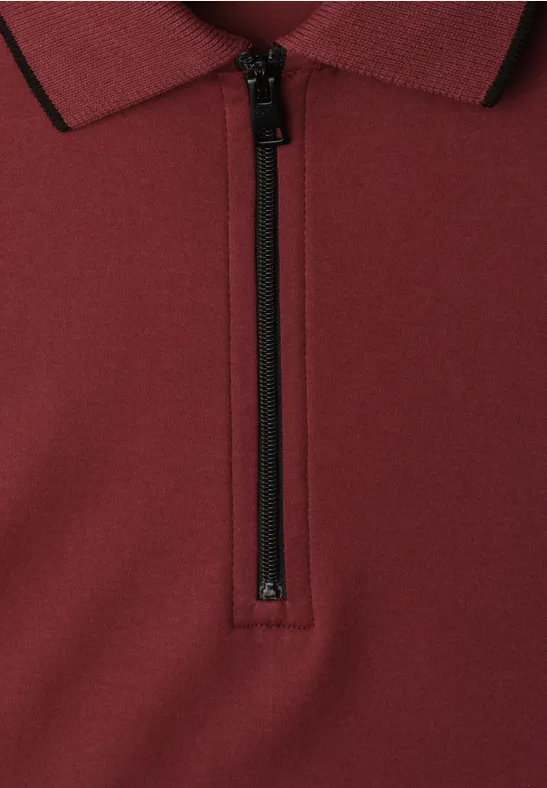 Nahaufnahme eines burgunderfarbenen Poloshirts mit halbhohem Reißverschluss und schwarzem Besatz.