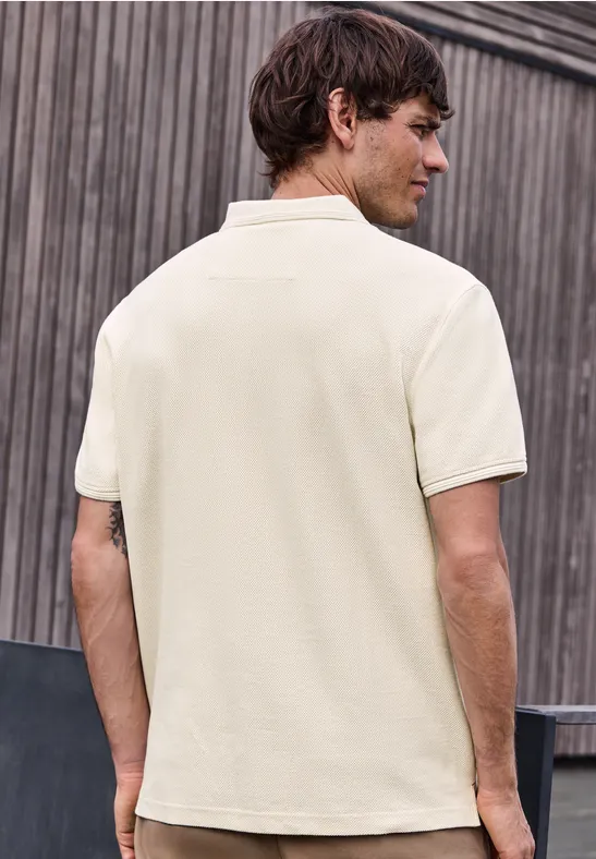Ein Mann von hinten in einem beigen Poloshirt vor einer Holzverkleidung.