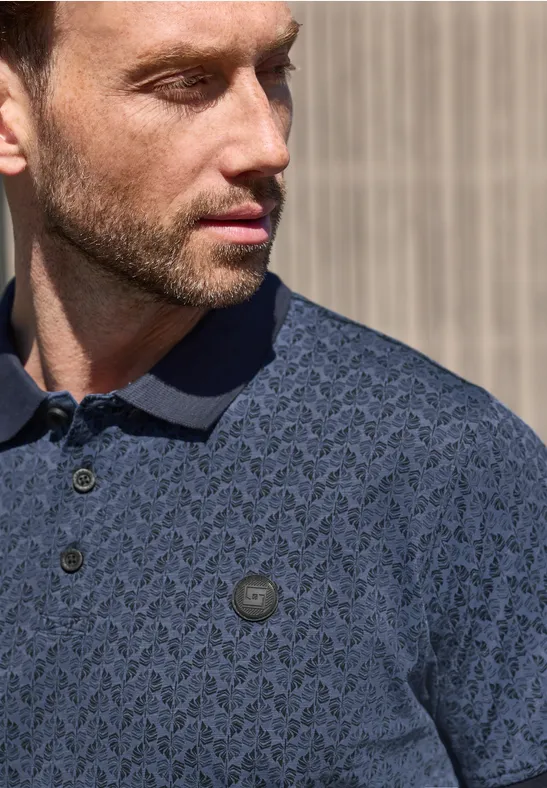 Een man kijkt opzij en draagt een donkerblauw polo met een subtiel patroon.