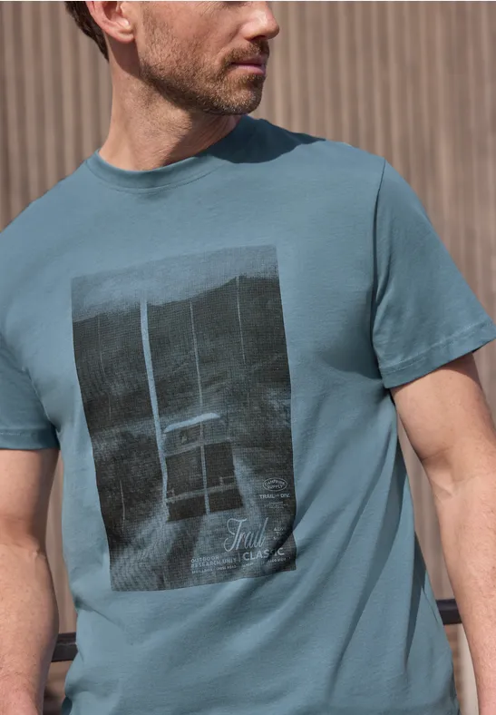 Seitlich abgebildeter Mann im türkisfarbenen T-Shirt mit schwarzem Rechteck-Print.