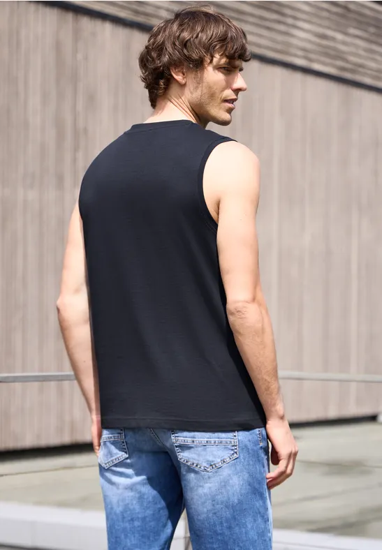 Mann mit schwarzem ärmellosem Shirt und blauen Jeans steht von hinten vor moderner Fassade.