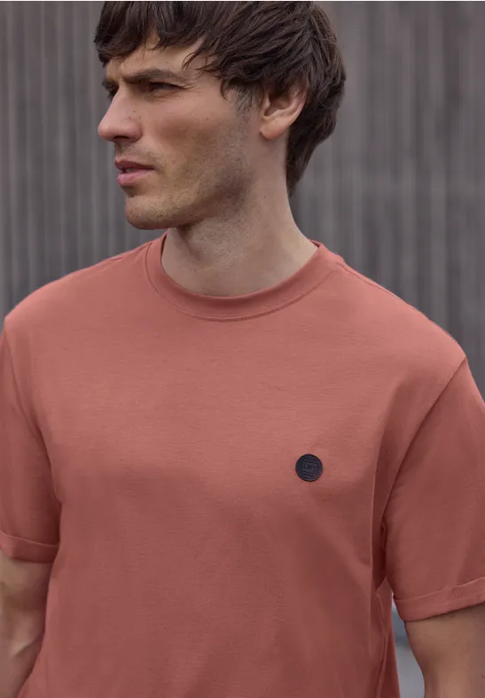 Ein verschwommenes Porträt einer Person in rostfarbenem T-Shirt vor einer grauen, vertikal gestreiften Wand.