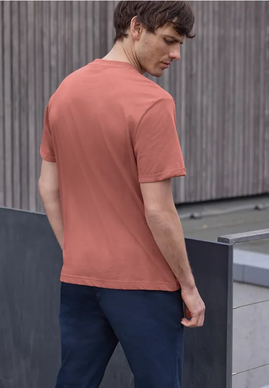 Ein Mann steht von hinten in rotem T-Shirt und dunkler Hose vor einer Holzfassade.