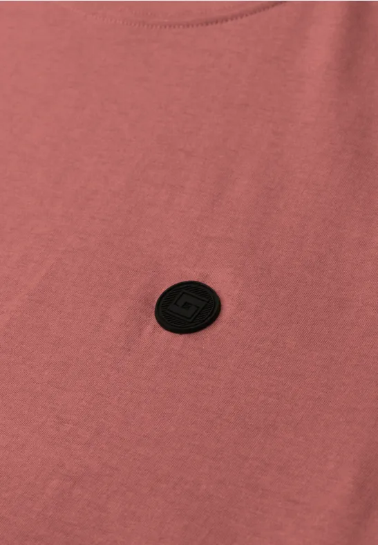 Rosa T-Shirt mit rundem schwarzen Logo-Patch auf der Brust.