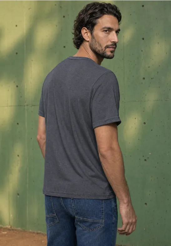 Mann in grauem T-Shirt und Jeans steht vor grünem Hintergrund und blickt über die Schulter.