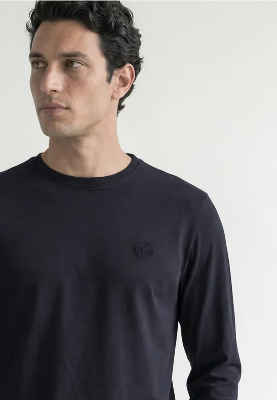 Mann blickt seitlich, trägt dunkelblaues Langarmshirt mit dezentem Logo.