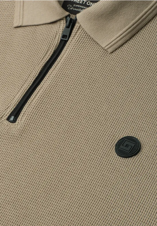 Beige Strick-Polo mit Reißverschluss und rundem schwarzem Logo-Emblem.