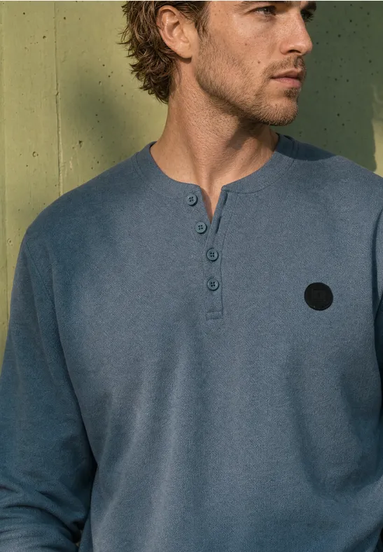 Ein Mann trägt ein langärmeliges, dunkelblaues Henleyshirt mit Knopfleiste.