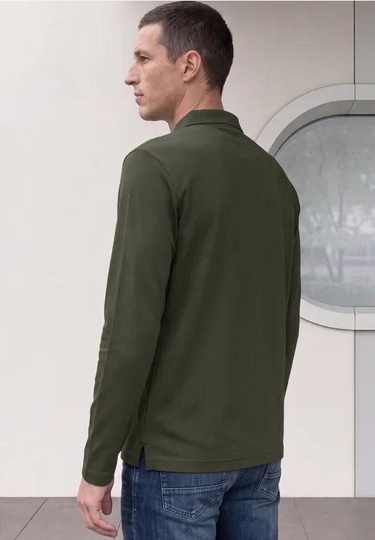 Mann von hinten in dunkelgrünem Langarm-Polo und Jeans vor hellem Hintergrund mit rundem Fenster.