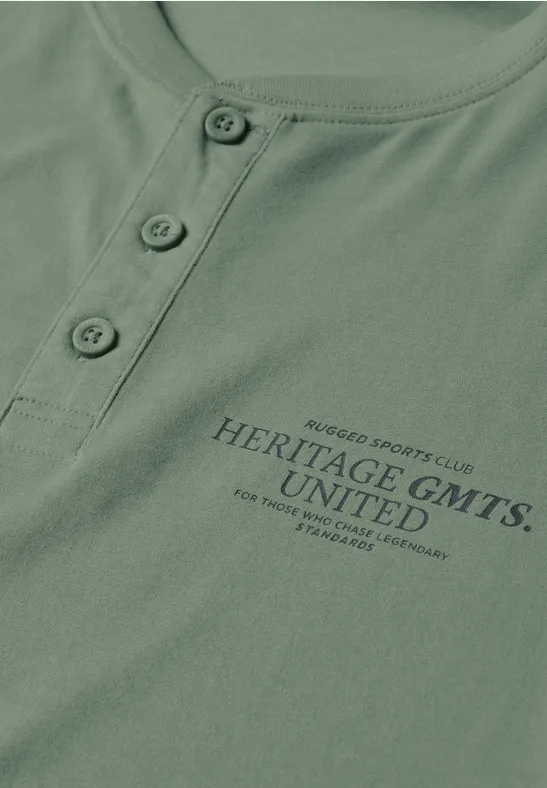 T-shirt vert avec patte de boutonnage et inscription 'HERITAGE GMTS. UNITED'