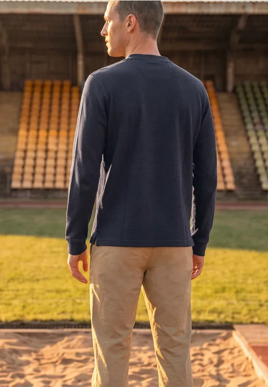Ein Mann steht mit dem Rücken zur Kamera auf einer Sportanlage vor Tribünen.