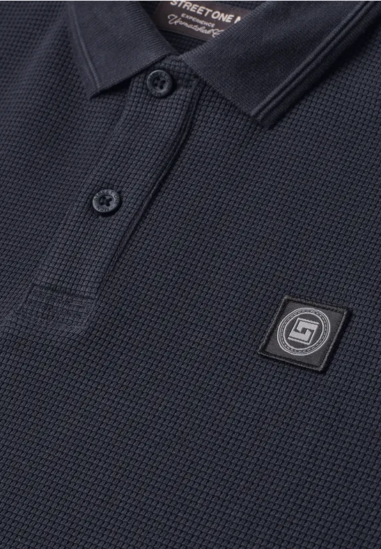Nahaufnahme eines dunkelblauen Polo-Shirts mit Kragen, zwei Knöpfen und einem quadratischen Logo-Badge.