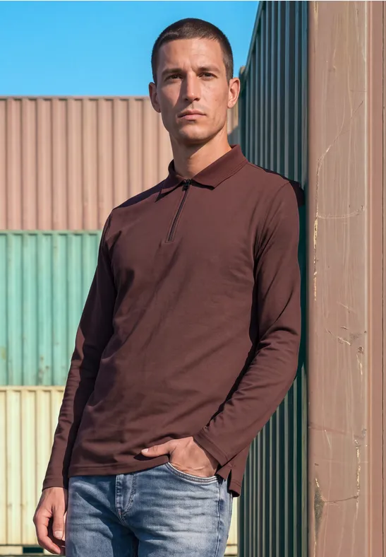 Ein Mann im dunkelroten Langarm-Poloshirt steht vor bunten Containern und blickt in die Kamera.