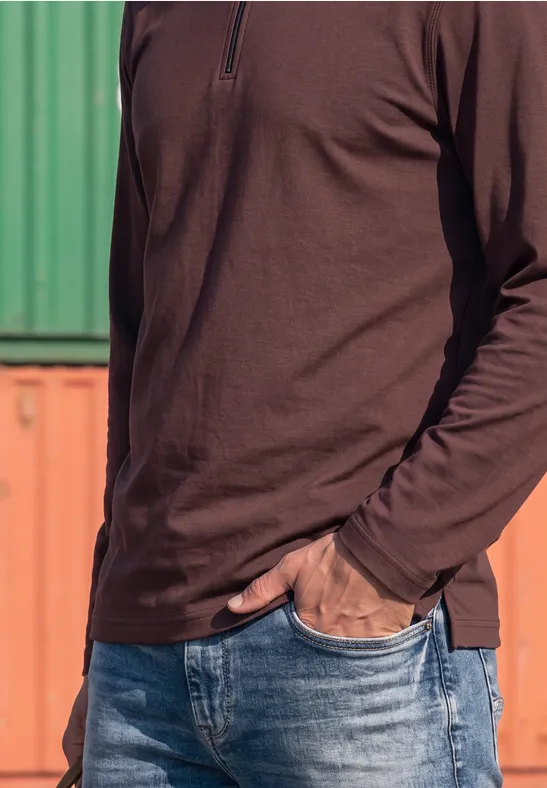 Teilansicht einer Person in braunem Langarmshirt und blauen Jeans vor farbigen Containern.