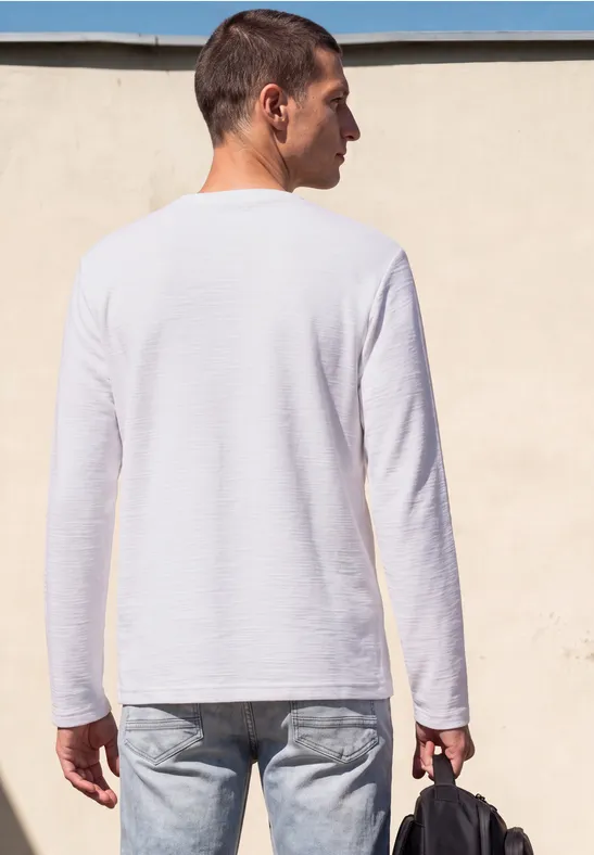 Ein Mann von hinten in weißem Langarmshirt und Jeans, trägt eine schwarze Tasche.