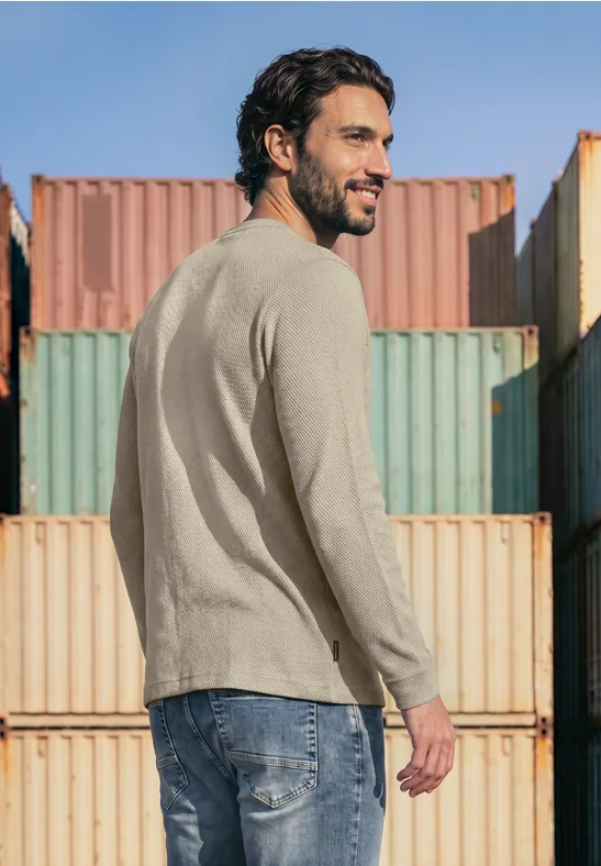 Een man in casual kleding staat voor gekleurde containers en kijkt over zijn schouder.