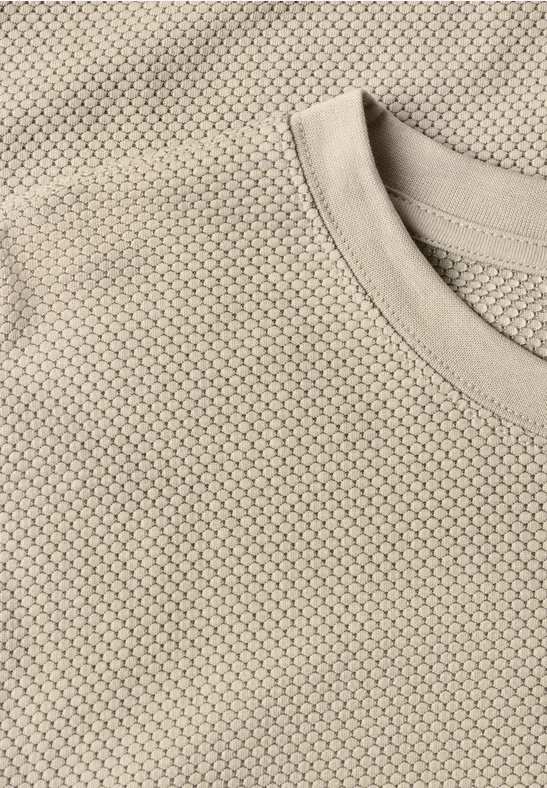 Close-up van een beige T-shirt met fijne honingraatstructuur.