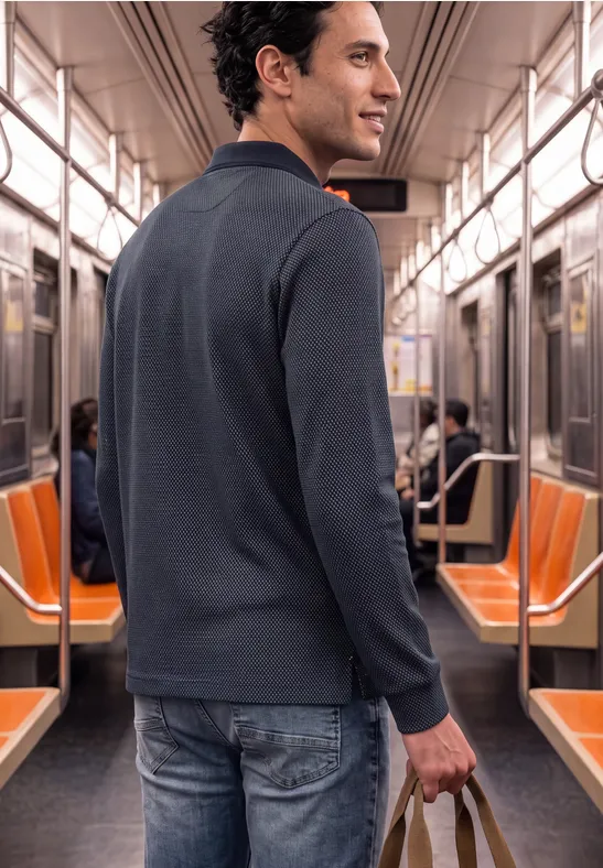 Mężczyzna w metrze ma ciemny sweter i dżinsy, trzyma butelkę.