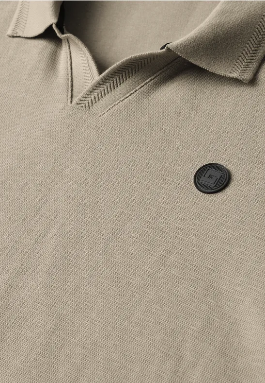 Close-up van een beige poloshirt met kraag en zwart rond logo, benadrukt textuur van de stof.