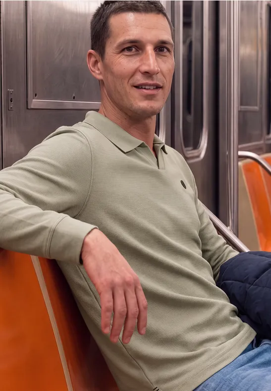 Een lachende man zit in de metro op oranje stoelen.