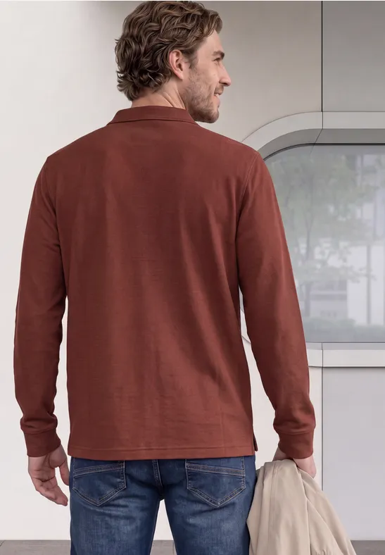 Een man gezien van achteren draagt een bruin langermig shirt en houdt nonchalant een jas vast.