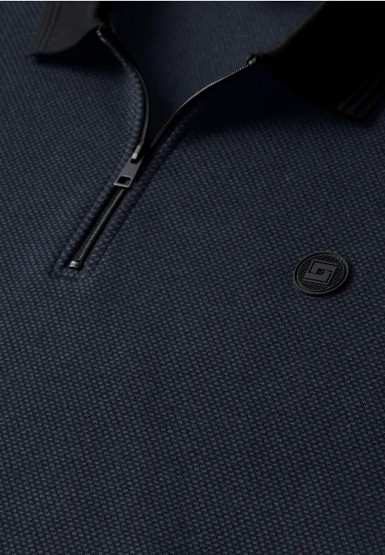 Detail eines dunkelblauen, strukturierten Polos mit halbem Reißverschluss und rundem Logo auf der Brust.