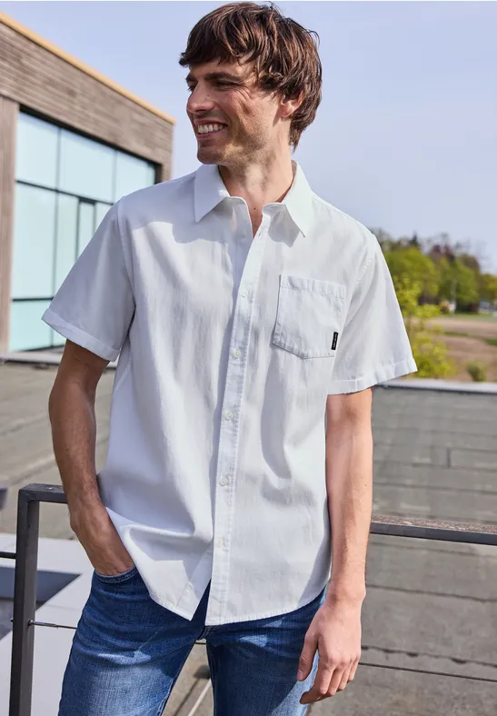 Mężczyzna w białej koszuli z krótkim rękawem i dżinsach stoi na tarasie.