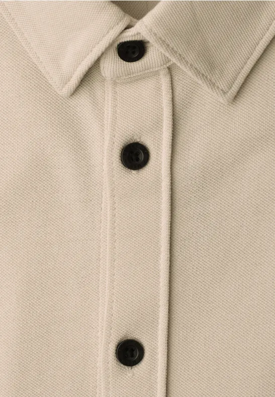 Beige Jacke mit Kragen und drei schwarzen Knöpfen in Nahaufnahme.