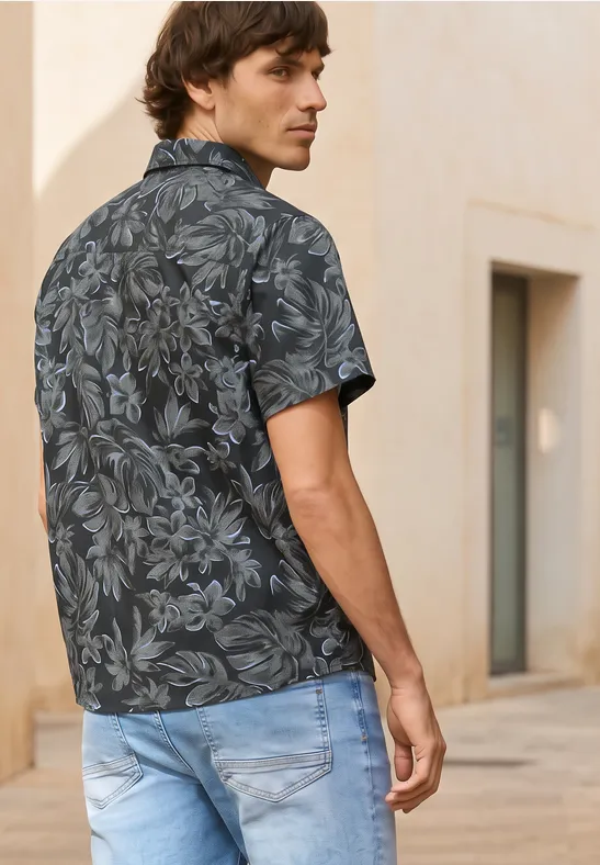 Ein Mann von hinten in einem schwarzen floralem Hemd und hellblauen Jeans steht vor einem Gebäude.