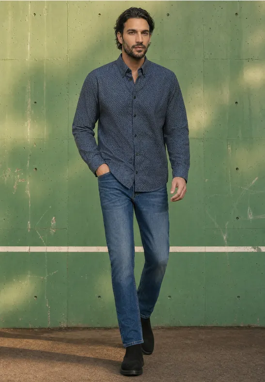 Ein Mann in dunkelblauem Hemd und Jeans steht lässig vor einer grünen Wand