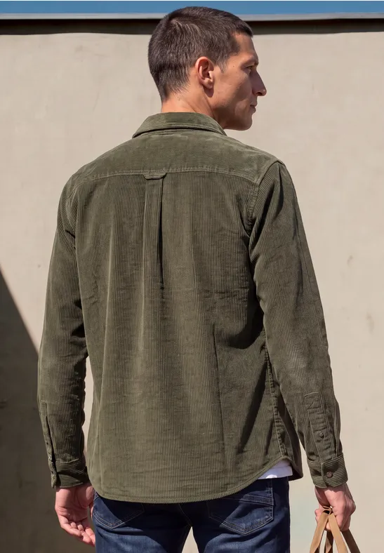 Achteraanzicht van een man in een kaki corduroy overhemd, nonchalant staand, kijkt opzij.
