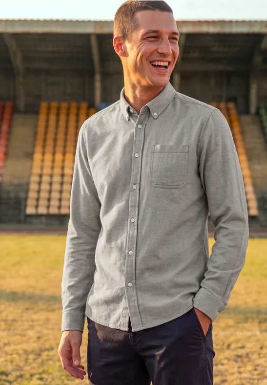 Ein freundlicher Mann in grauem Hemd lächelt vor leeren Tribünen im Stadion.