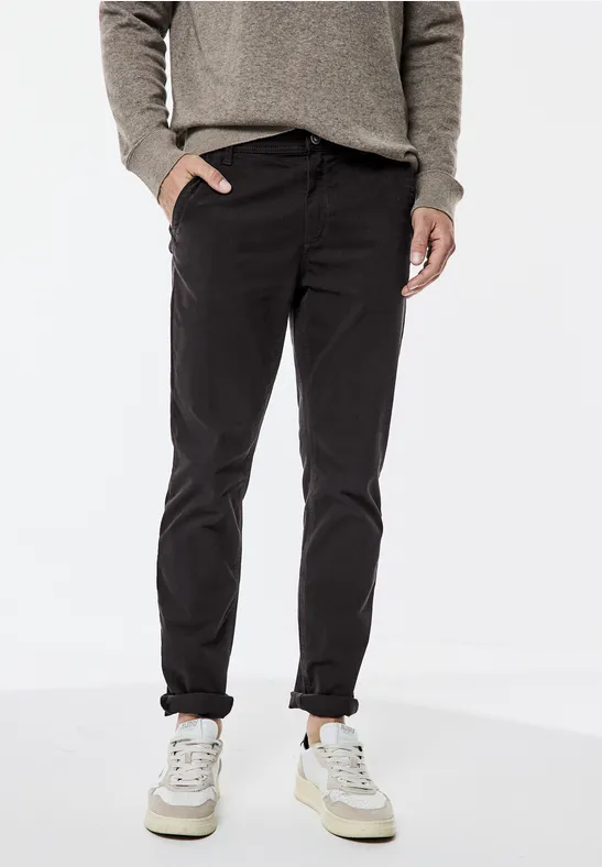 Mann trägt dunkle Hose, Pullover und weiße Sneakers.