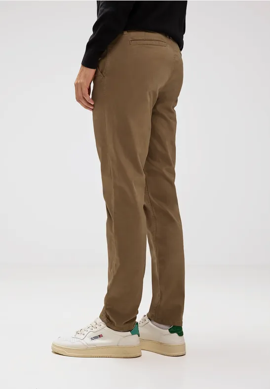 Person trägt braune Hose und weiße Sneaker, steht seitlich im Studio.