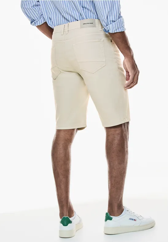 Mann in beiger kurzer Hose und weiß-grünen Sneakers, Hemd mit Streifen, Rückenansicht.