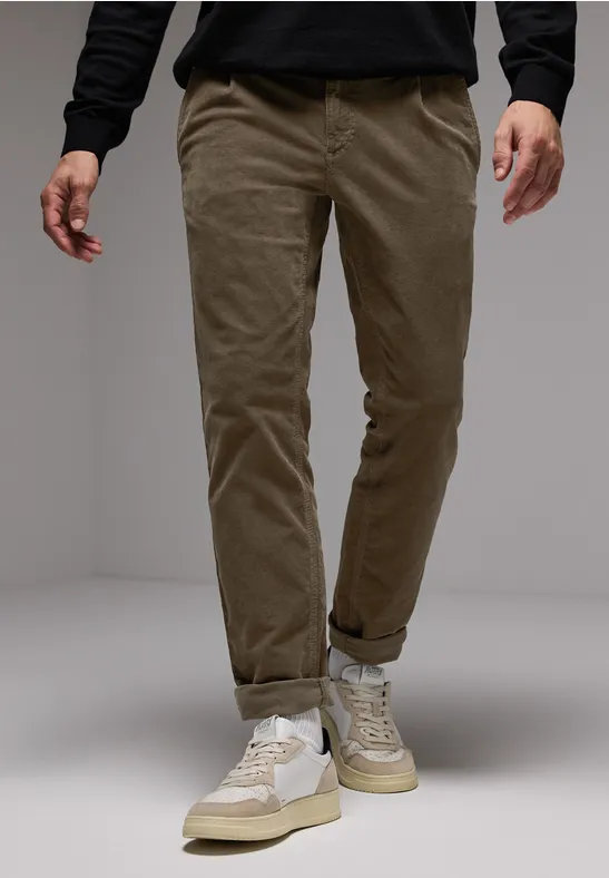 Homme en pantalon beige, sneakers blanches, pull noir.
