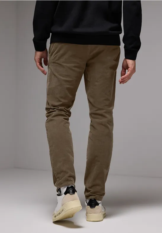 Personne en pantalon marron et baskets blanches debout.