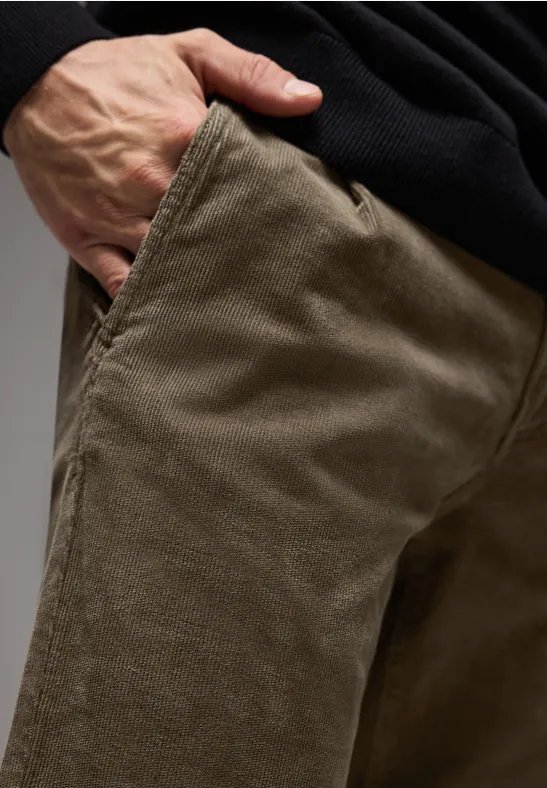 Main dans la poche d’un pantalon en velours brun.