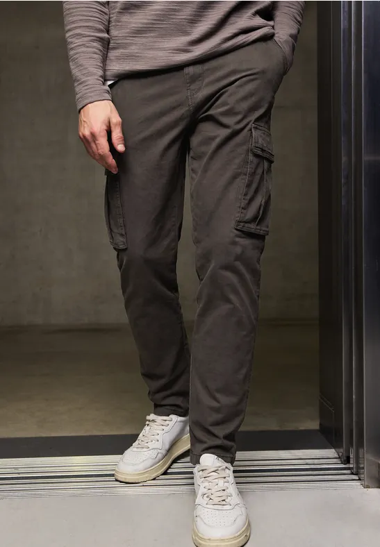 Person trägt graue Cargohose und weiße Sneaker, steht in einem Aufzug.