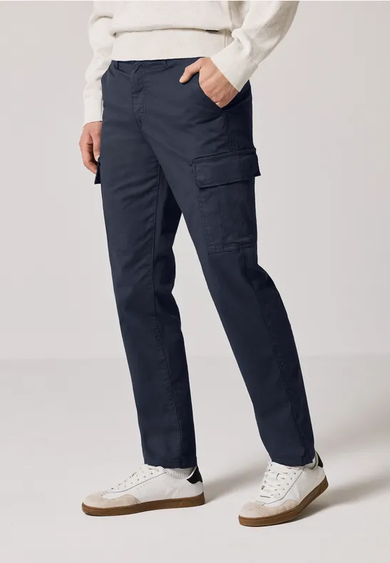 Person trägt dunkelblaue Cargohose und weiße Turnschuhe.