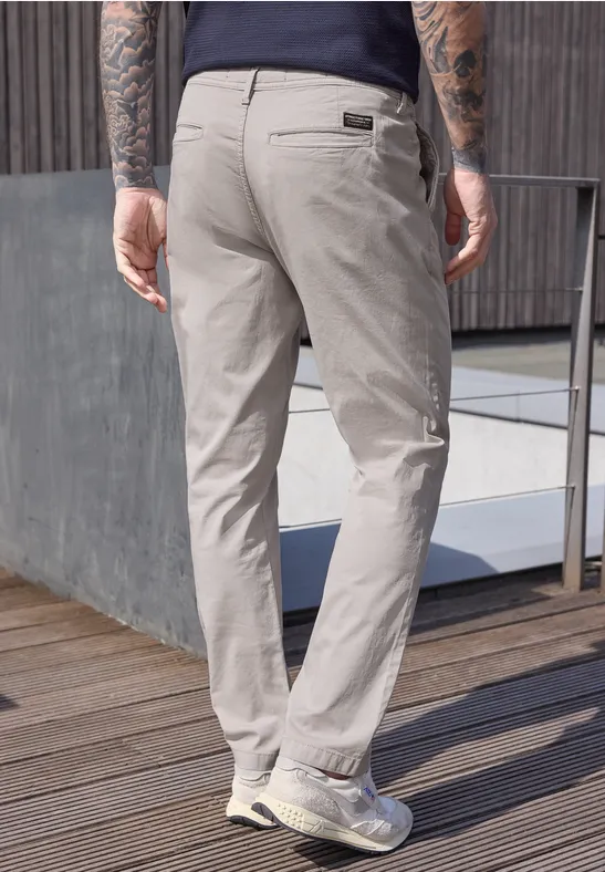 Un homme vu de dos porte un pantalon chino clair sur une terrasse en bois près d’une balustrade.