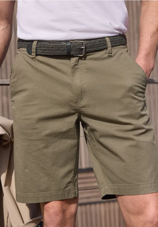 Unterkörper einer Person in olivgrünen Shorts mit geflochtenem Gürtel, Hände in den Taschen.