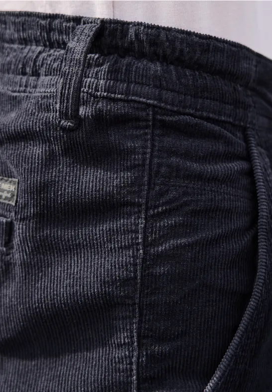 Nahaufnahme einer schwarzen Cordhose mit elastischem Bund und Gürtelschlaufen.