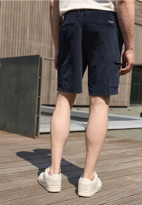 Mann von hinten in marineblauen Cargo-Shorts und weißen Sneakers auf Holzdeck.