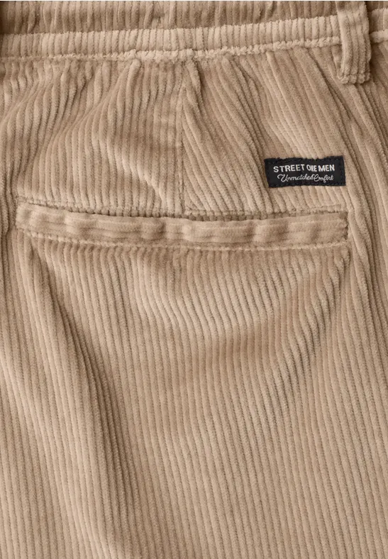 Close-up van beige corduroy broek met achterzak en klein zwart label 'STREET MOTOR'.
