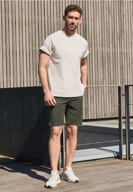 Een man in een wit T-shirt en groene korte broek staat op een houten terras bij een balustrade.
