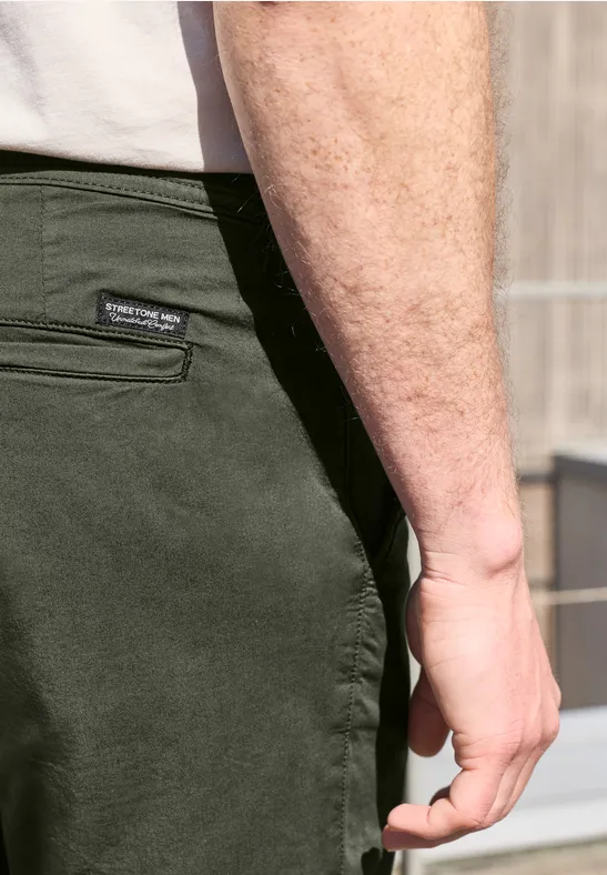 Close-up van een man in olijfgroene broek en wit T-shirt, met de hand naast de heup.