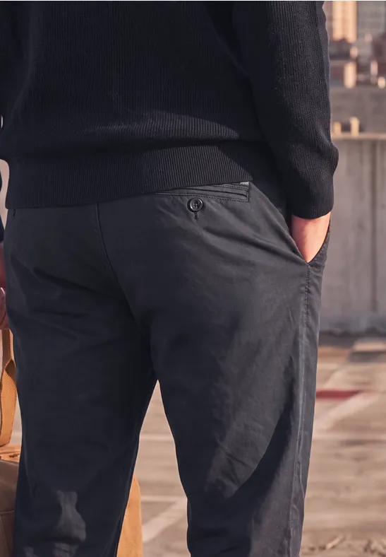 Nahaufnahme eines Mannes von hinten in dunkelgrauen Hosen mit Händen in den Taschen auf einem Dach