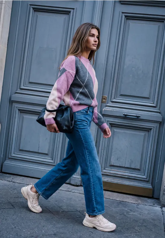 Eine Frau in buntem Pullover, Jeans und Sneakers geht an einer großen grauen Tür vorbei.